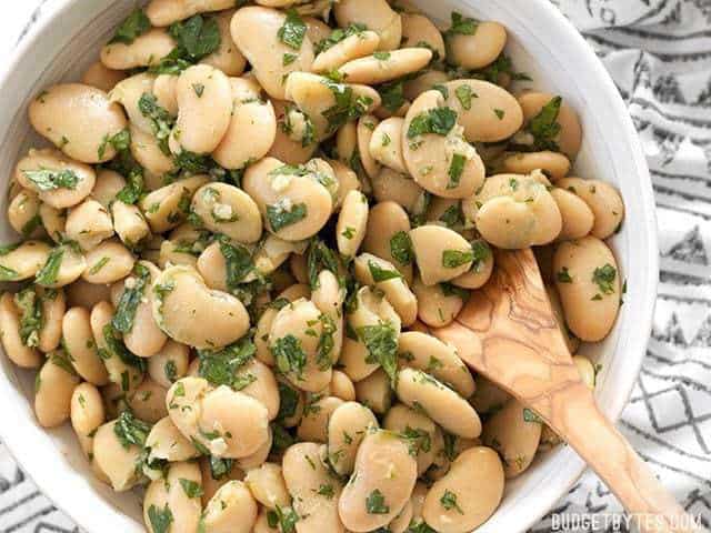 Close-up of marinated white beans in a bowl with a wooden spoon.