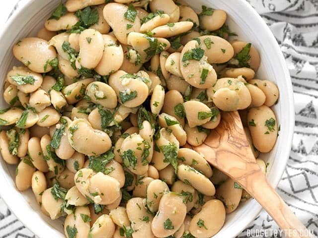 Top view of Marinated White Beans in white bowl with wooden serving spoon 