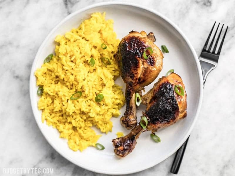 Two chicken adobo drum sticks with a side of rice plated on a white plate