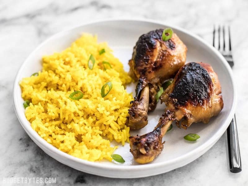 two chicken adobo drum sticks with a side of rice plated on a white plate 