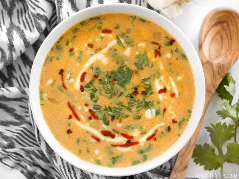 Spicy coconut pumpkin soup in a bowl with a wooden spoon.