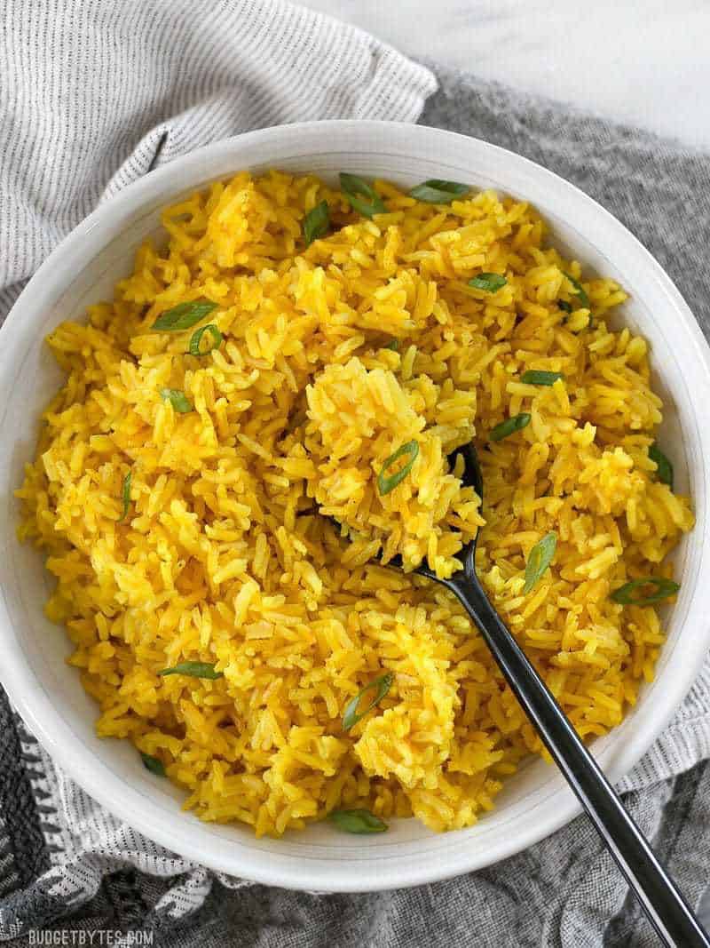 Overhead view of a large bowl of Yellow Jasmine Rice with green onion sprinkled over top and a black spoon.