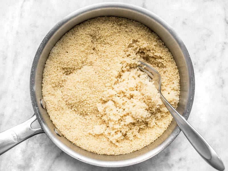 Cooked couscous being fluffed with a fork