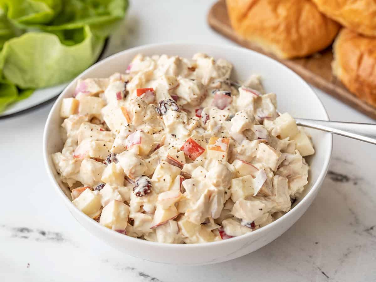 Side view of a bowl of chicken salad with apples, croissants in the background