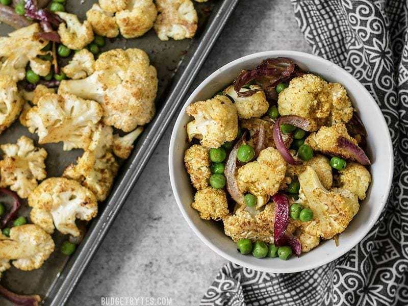 A bowl of Curry Roasted Cauliflower next to the roasting sheet pan and a black and white napkin.