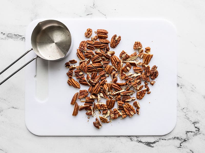 Chopped pecans on a cutting board with measuring cup