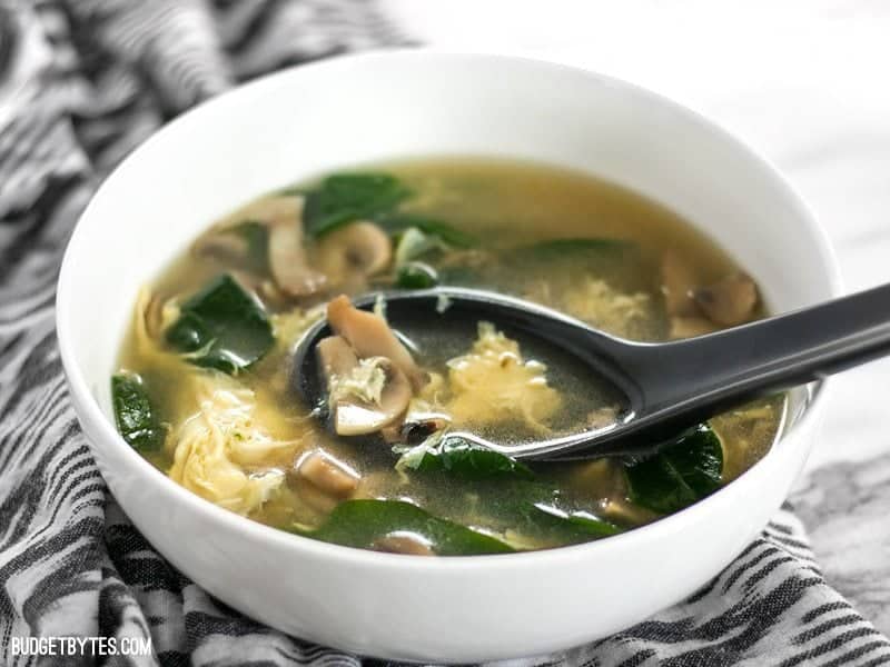 front view of a bowl of homemade easy egg drop soup with a black ceramic soup spoon