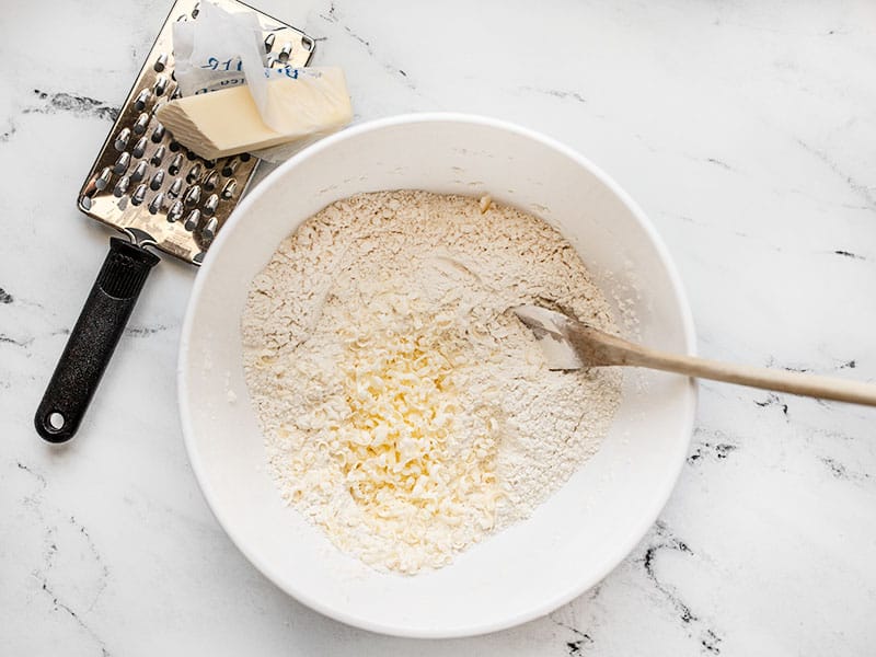 Grated frozen butter added to bowl of dry ingredients, cheese grater on the side