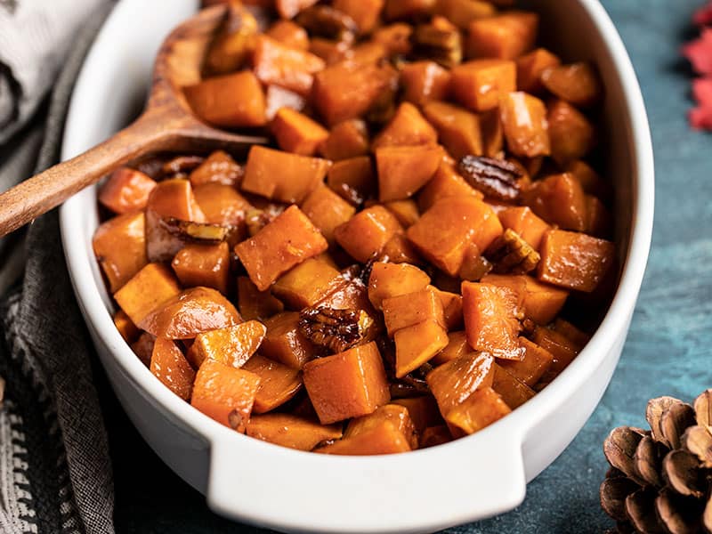 Front view of the casserole dish full of Maple Roasted Sweet Potatoes with Pecans with pine cones on the side