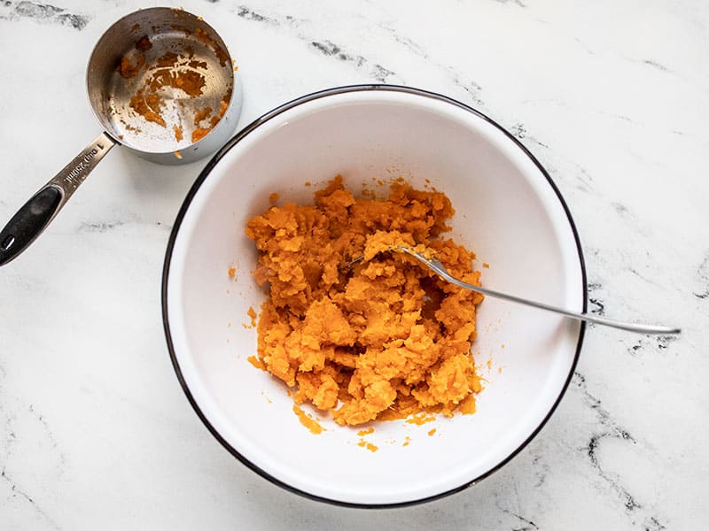 one cup of mashed sweet potato in a bowl, a measuring cup on the side