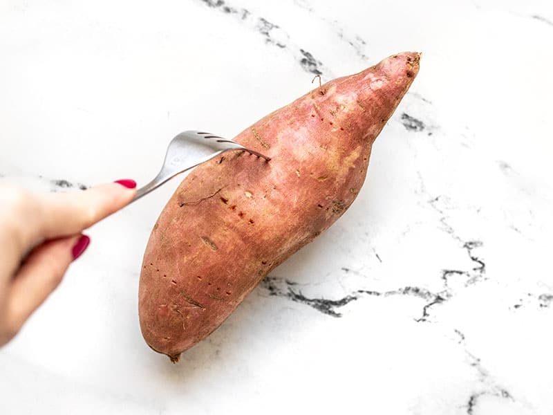 A fork pricking a raw sweet potato