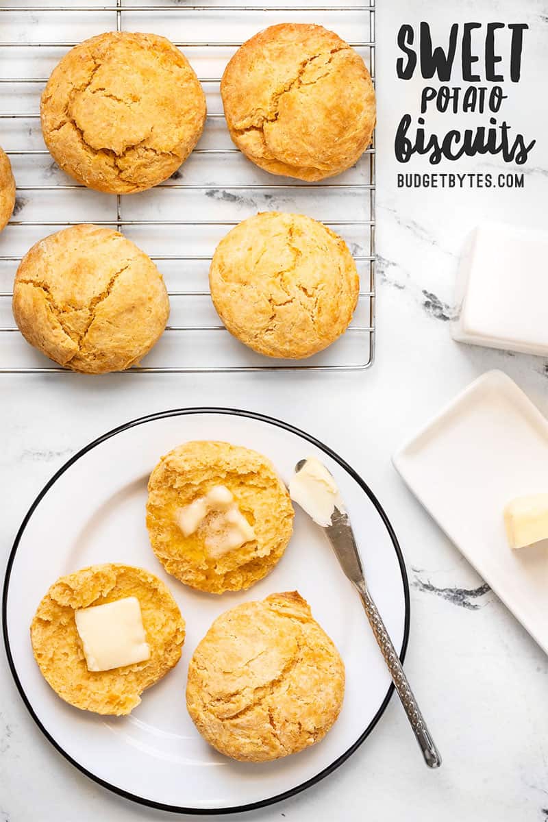 Sweet potato biscuits on a wire cooling rack and on a plate, one open with butter on top.