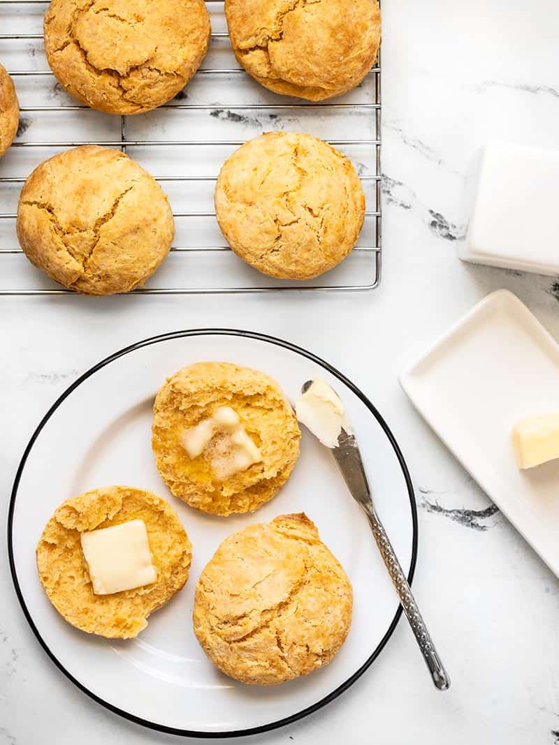 Sweet Potato Biscuits on a wire cooling rack and a couple biscuits on a plate, one open and smeared with butter