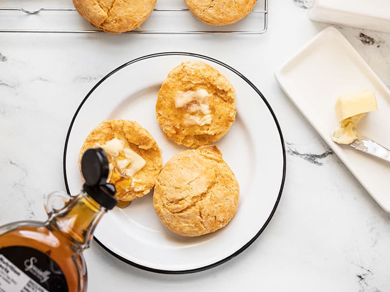 Maple syrup being poured onto a buttered sweet potato biscuit