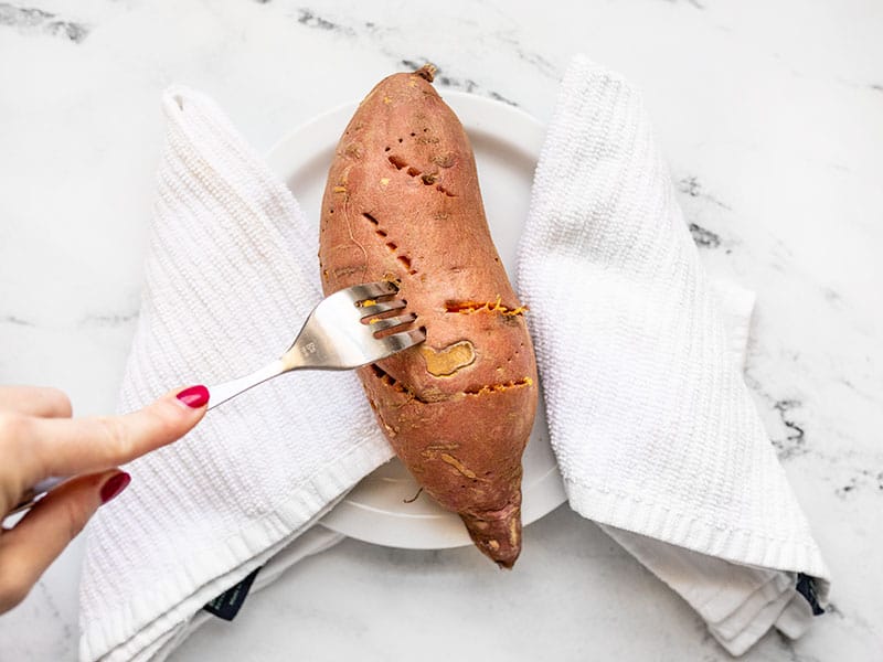 Fork poking a cooked sweet potato on a plate