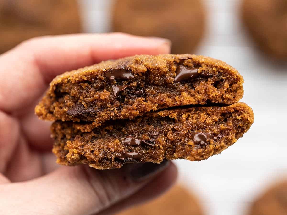 A hand holding a chocolate molasses cookie broken in half