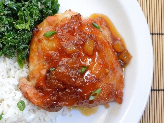 Close-up of teriyaki chicken with pineapple, served with kale and rice on a plate.