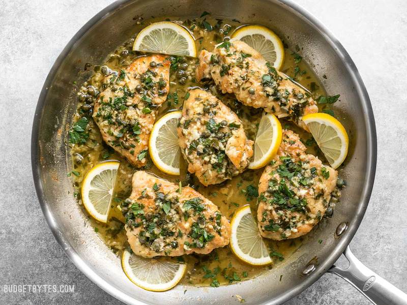 A skillet of prepared Chicken Piccata with lemon garlic sauce and capers.