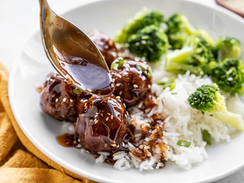 Close up of teriyaki meatball bowls with sauce being drizzled over top