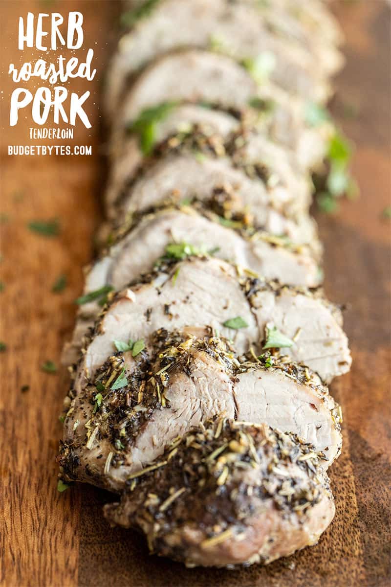 front view of slices of herb roasted pork tenderloin on a wooden cutting board, title text overlay at the top