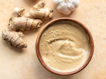 A wooden bowl filled with sesame ginger dressing next to a knob of fresh ginger