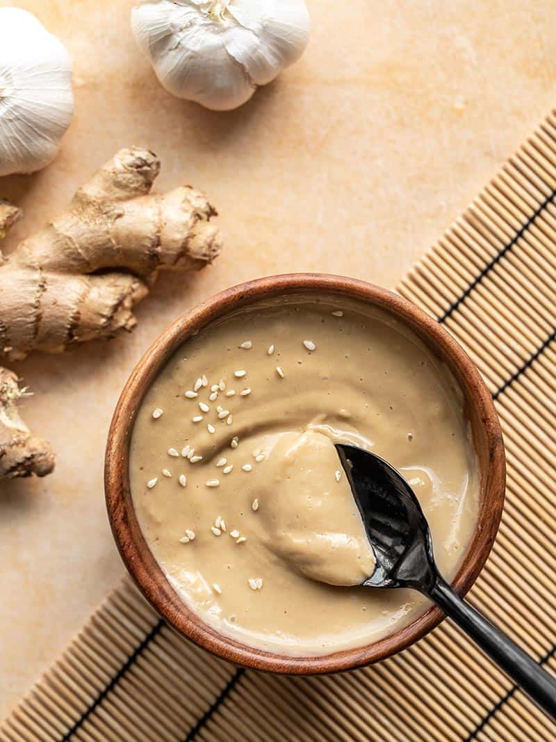 Sesame ginger dressing in a wooden bowl, garnished with sesame seeds, a spoon in the middle of the bowl.