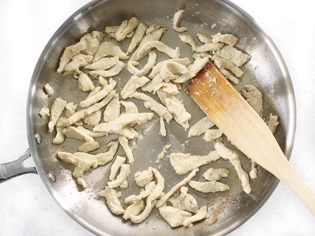 Cooked Chicken strips in the skillet with a wooden spatula