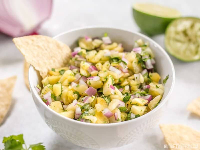 Front view of a bowl of easy pineapple salsa with a tortilla chip stuck in the side of the bowl