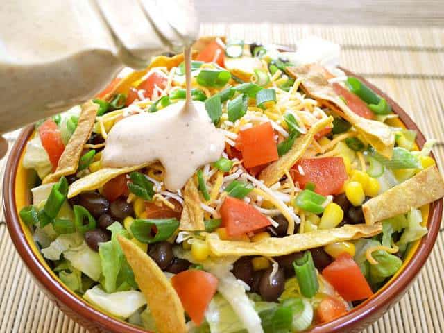 Pouring taco ranch dressing into a bowl of southwest salad.