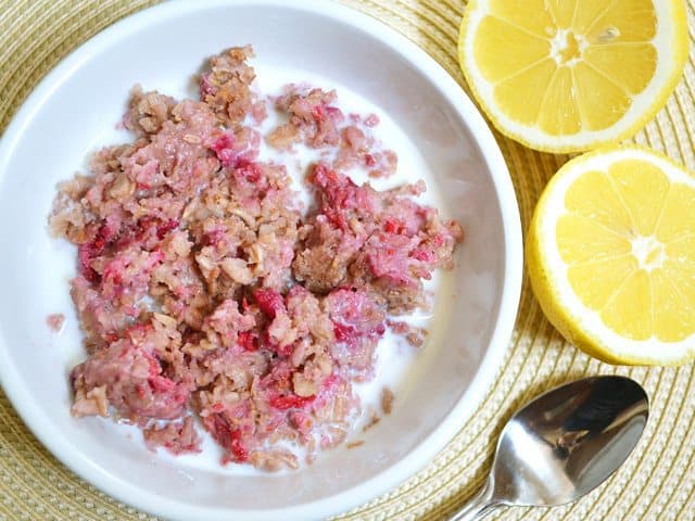 Creamy lemon raspberry oatmeal in a bowl with a spoon and lemons.