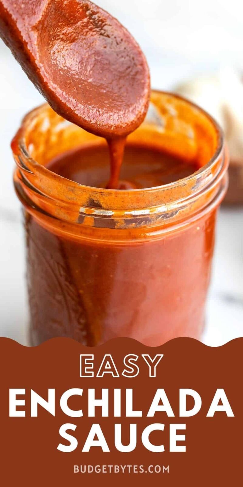 Enchilada sauce dripping off a wooden spoon into a glass jar.