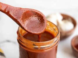 close up of enchilada sauce dripping off a wooden spoon into a jar.