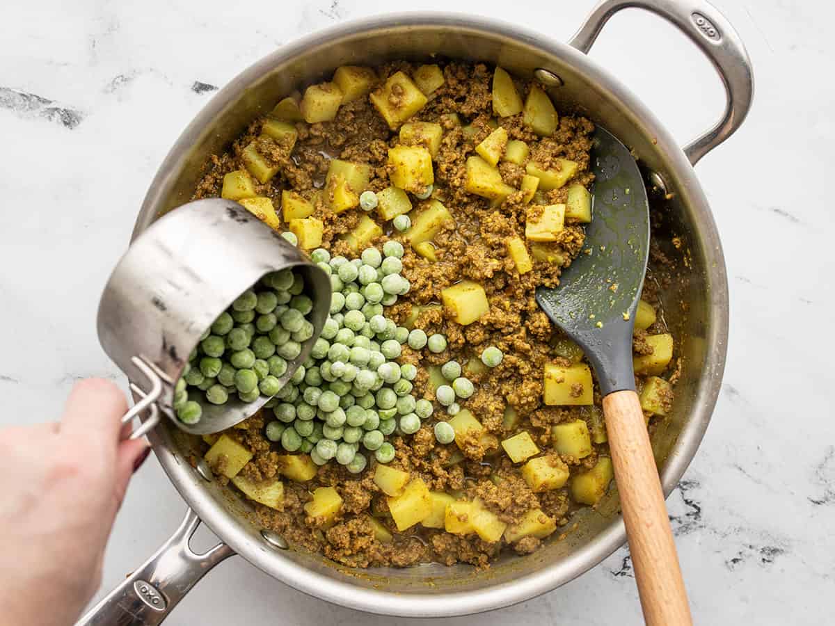 Frozen peas being poured into the skillet