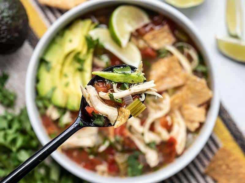 Close up of a spoonful of Chicken and Lime Soup with the bowl in the background.