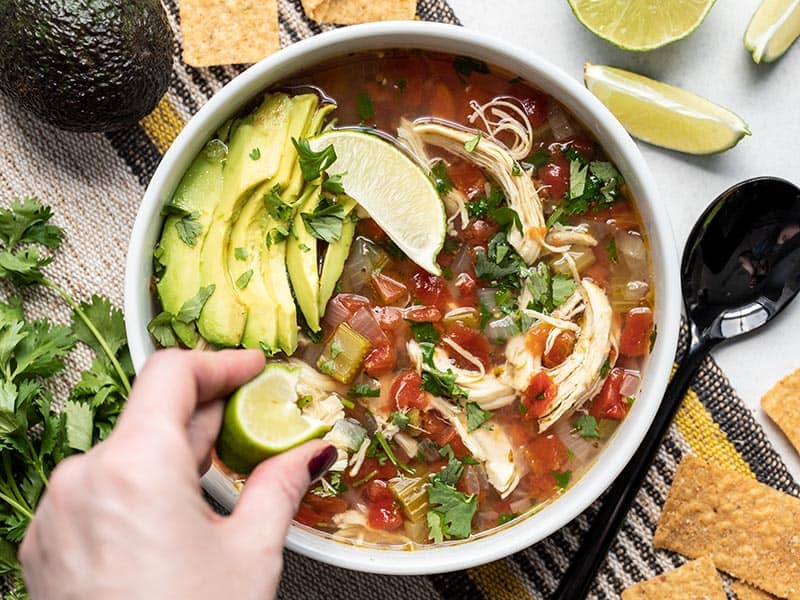 A hand squeezing a wedge of lime into a bowl of Chicken and Lime Soup