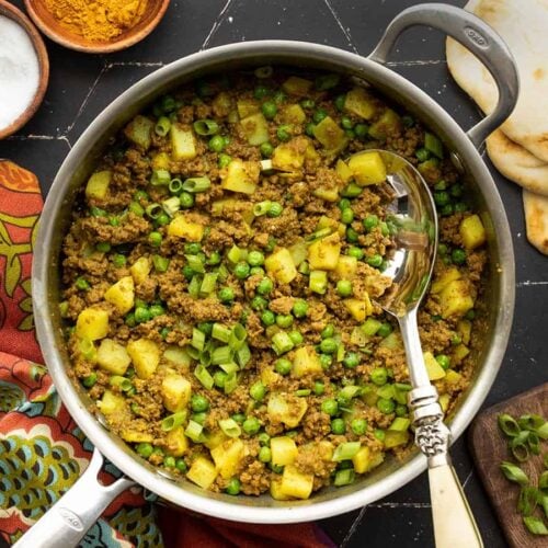 curried ground beef with peas and potatoes in a skillet with a serving spoon