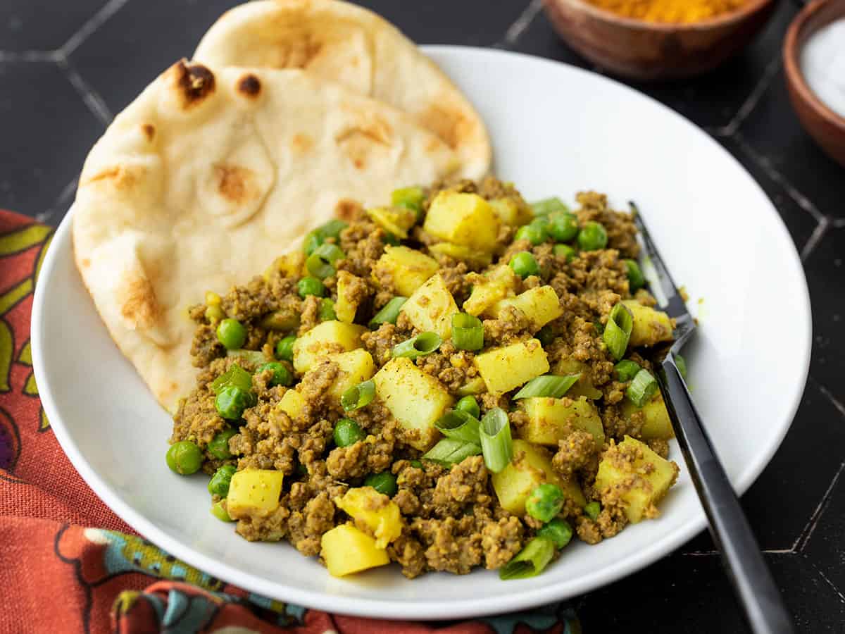 Side view of a bowl of curried beef with peas, naan in the side of the bowl