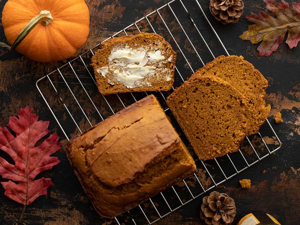 sliced loaf of pumpkin bread on a cooling rack with one slice smeared with butter