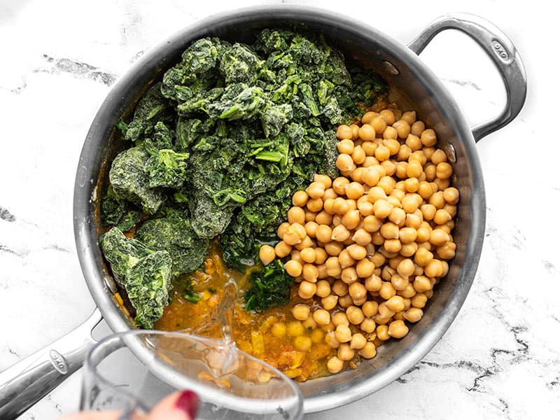 Frozen spinach, chickpeas, and water added to the skillet