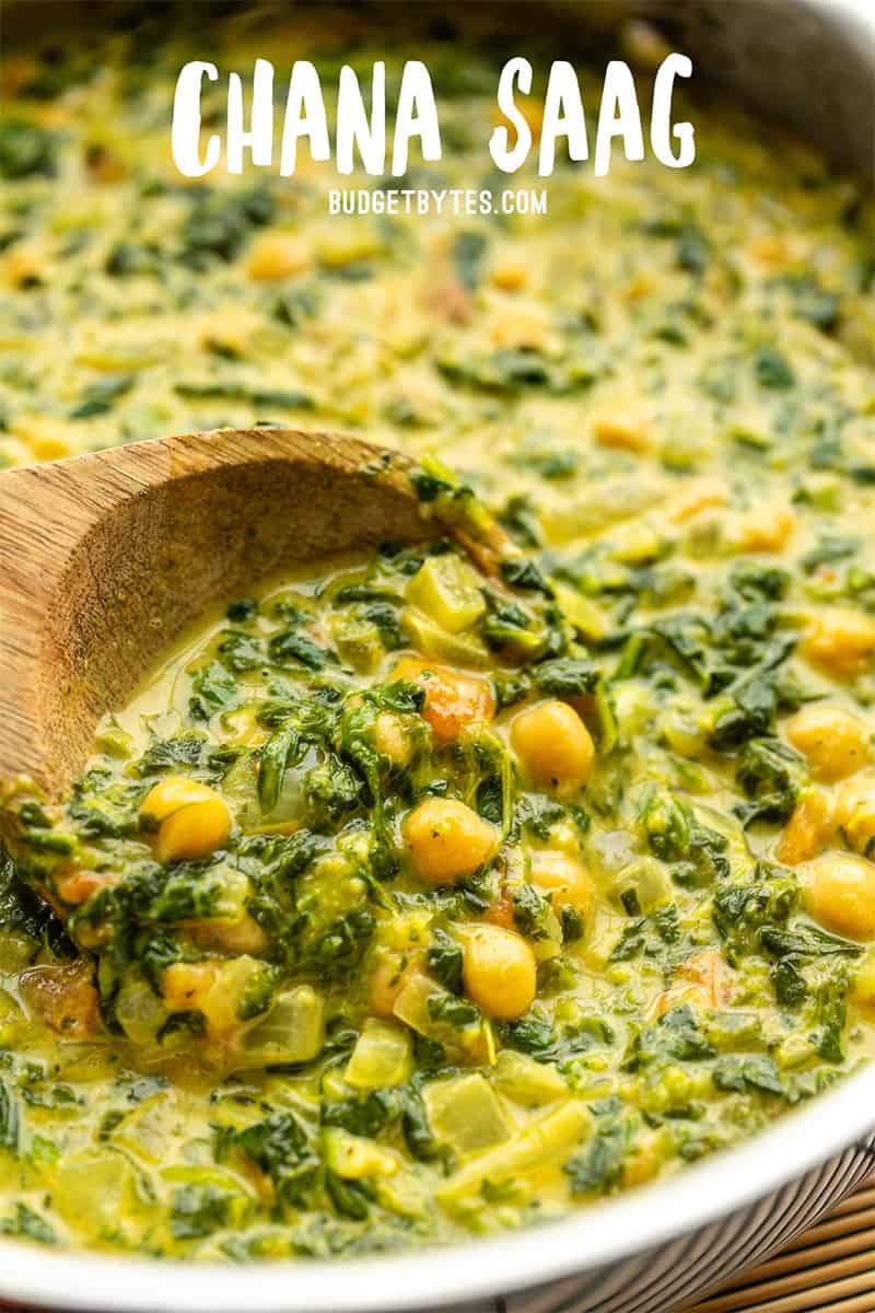 Close up of a wooden spoon scooping chana saag out of the skillet with title text at the top