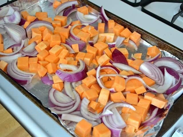 sweet potato and onion on baking sheet lined with tin foil, ready to roast 