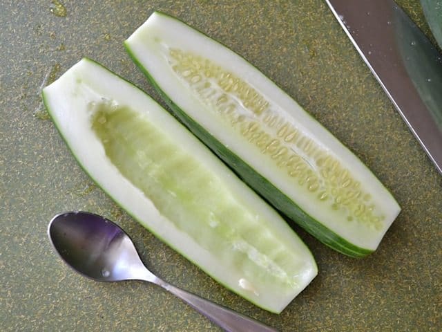 cucumber cut in half and removing seeds with spoon 