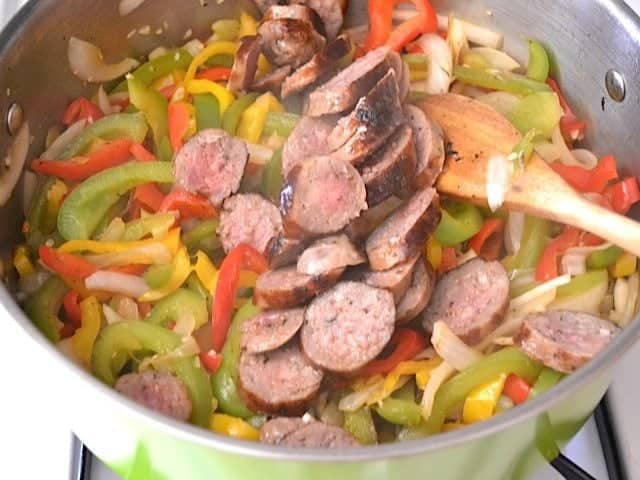 Adding sliced cooked sausage back to pot with onions and peppers 