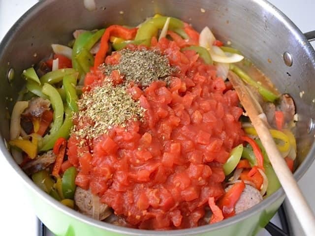 Tomatoes and herbs added to pot with other ingredients 