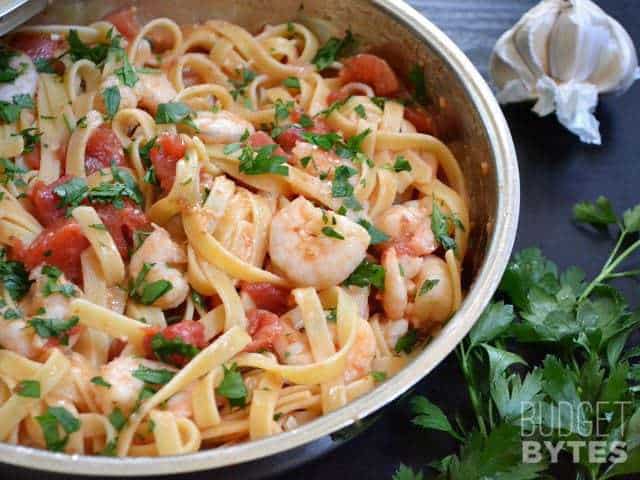 A skillet of spicy shrimp pasta garnished with herbs.