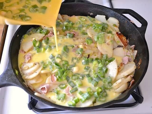 Pouring egg mixture onto potatoes in skillet 