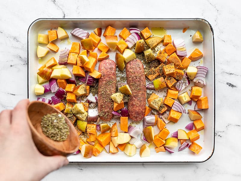 Diced apples, sweet potatoes, and sausage being seasoned with herbs