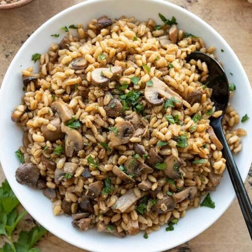 overhead view of baked barley with mushrooms in a serving bowl with a spoon