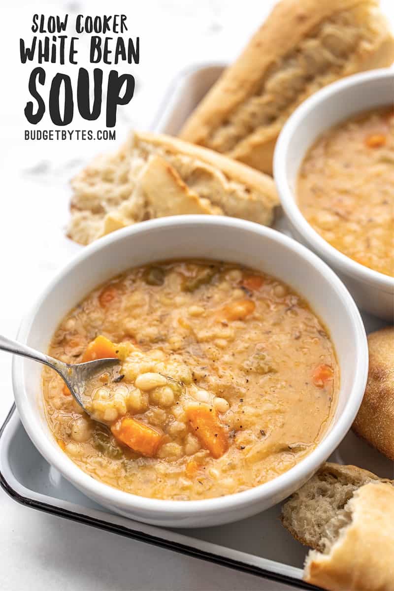 Front view of two bowls of white bean soup with a spoon lifting a bite out of the front bowl, title text at the top