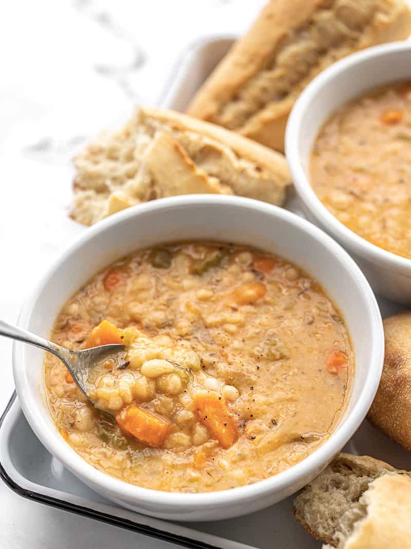 Front view of two bowls of slow cooker white bean soup on a tray, a spoon lifting a bite out of the front bowl